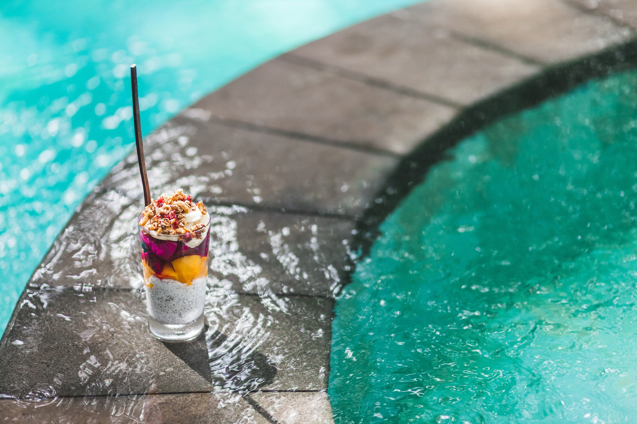 Coconut chia pudding coctail with fresh mango, banana and dragonfruit on edge of pool with clean turquoise water. Tropical style